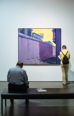 Besucher betrachten ein Gemälde, darauf die Berliner Mauer