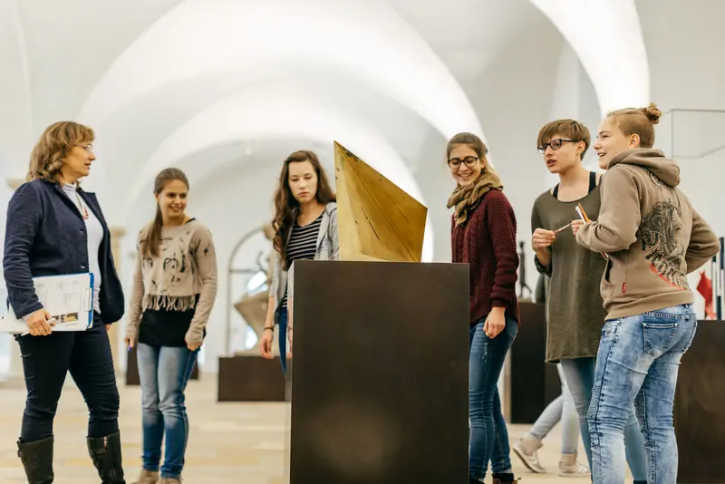 eine Gruppe Jugendlicher betrachtet eine geometrische Skulptur