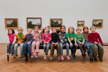 Kinder sitzen in einer Ausstellung auf einer Bank