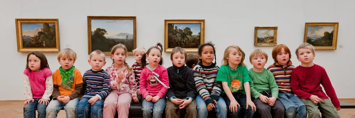 Kinder sitzen in einer Ausstellung auf einer Bank