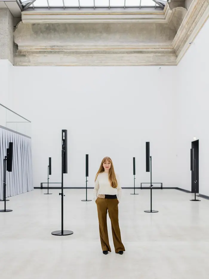 Eine Frau steht selbstbewusst in einem Ausstellungsraum 