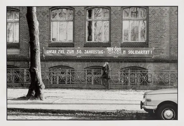 schwarz-weiß Fotografie mit einem Mietshaus, Baum und angeschnittenen Auto