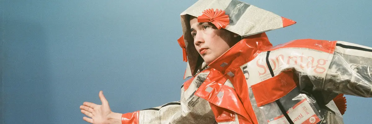 Frau in einem Kostüm aus Zeitungspapier vor blauem Hintergrund