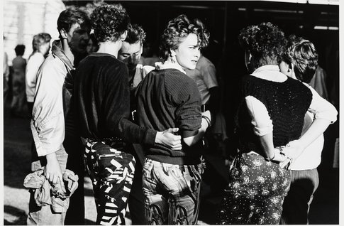 Schwarz-Weiß-Fotografie einer Gruppe, die mit den Rücken zum Betrachter steht, nur eine Frau blickt über die Schulter.