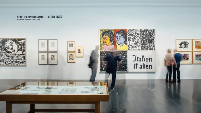 Eine Ausstellungsansicht mit abstrakten Gemälden und Besuchenden 