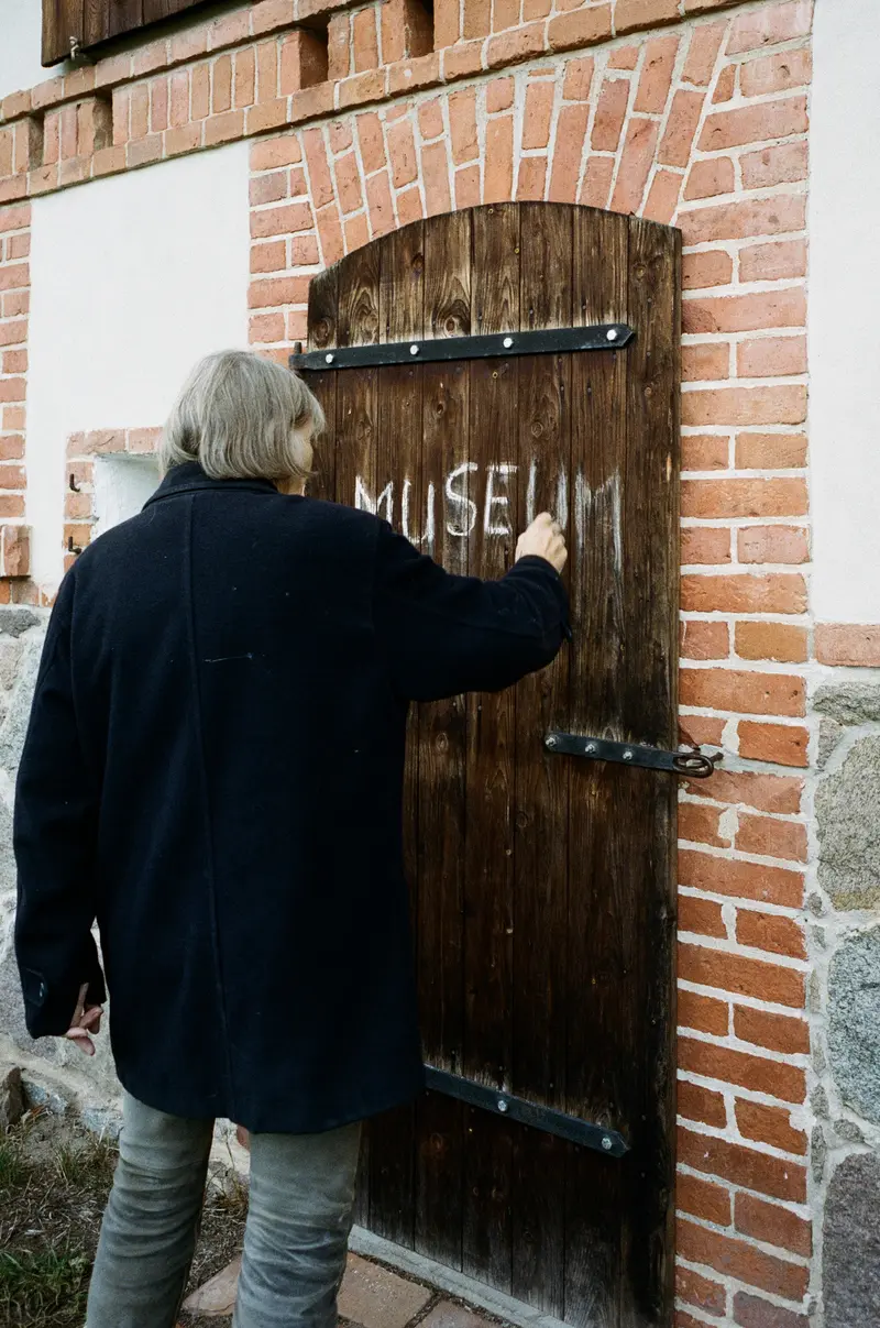 Frau in Rückenansicht schreibt mit Kreide "Museum" auf ein Scheunentor