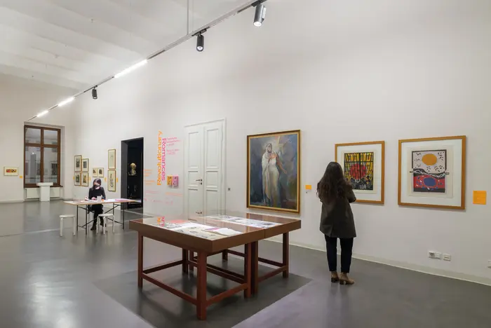 Eine Ausstellungsansicht mit Gemälden und Besucherinnen 