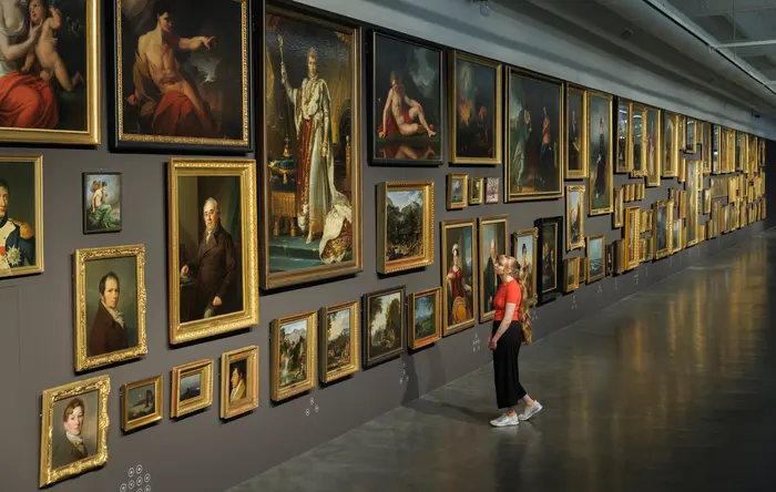 Frau schaut auf lange Wand mit vielen Gemälden